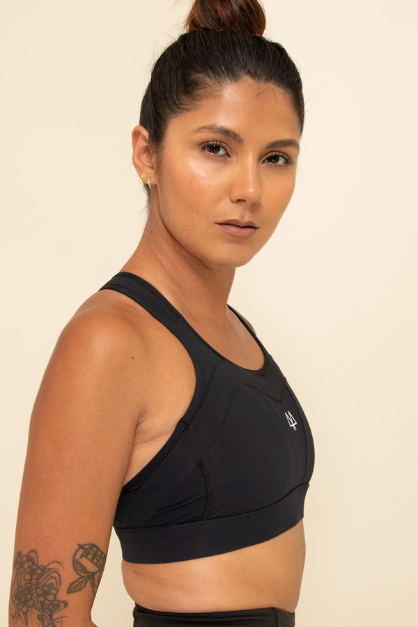 Woman wearing a supportive Black Sports Bra from a side view. The Overband Technology can be seen.